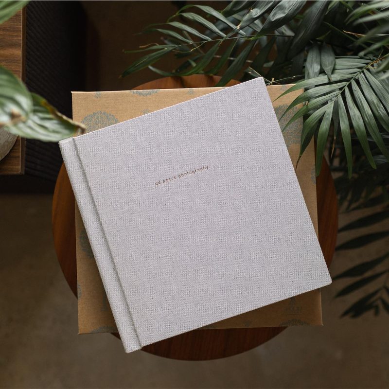 A eco friendly fine art wedding album in a fabric cover sitting on a box and next to green plants