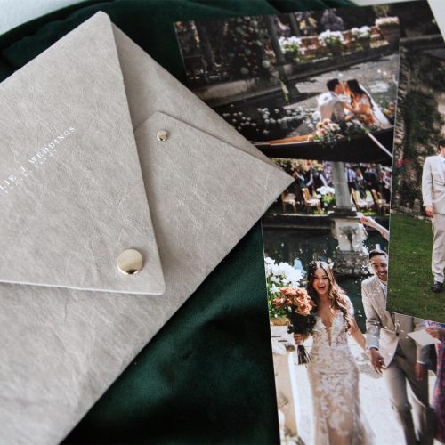 A stone coloured print delivery pouch with white printed personalisation and silver fastenings with a collection of wedding prints