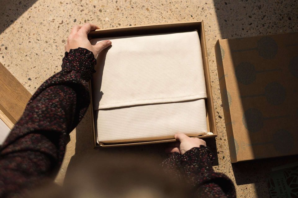 A fine art photo album in a natural cotton bag being taking out of a kraft presentation box
