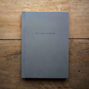 A grey leather portrait format wedding album from Folio Albums placed on a wooden floor viewed from above.