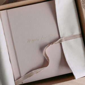 A blush pink luxury album with real gold cover text in a natural cotton wrap and ribbon
