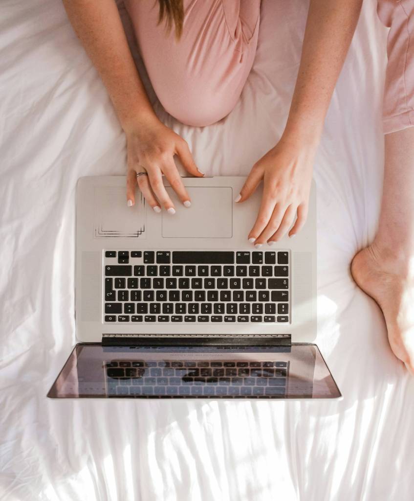 Hands of a woman sitting on a bed with a laptop