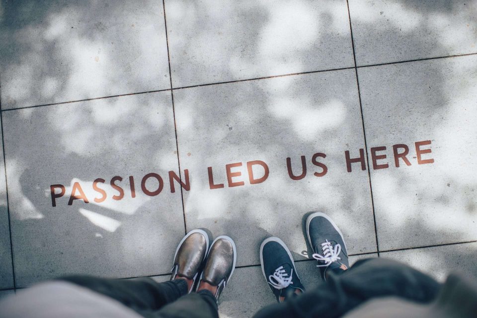 Looking down at feet on pavement with text Passion Lead Us Here