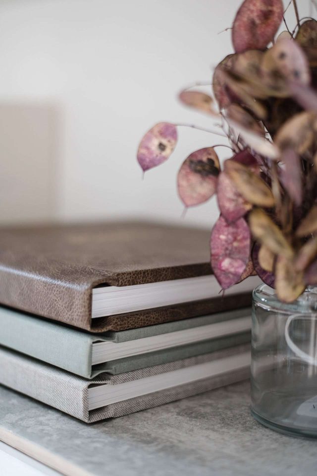 A stack of heirloom wedding albums with different cover materials including vintage leather and fabric