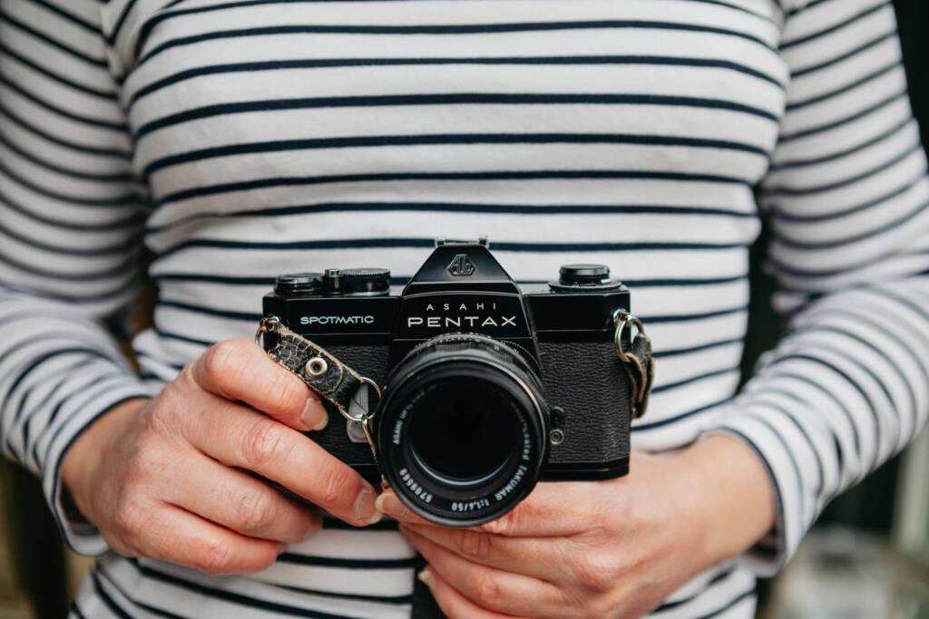 woman in striped told holding an old camera used to take photographs