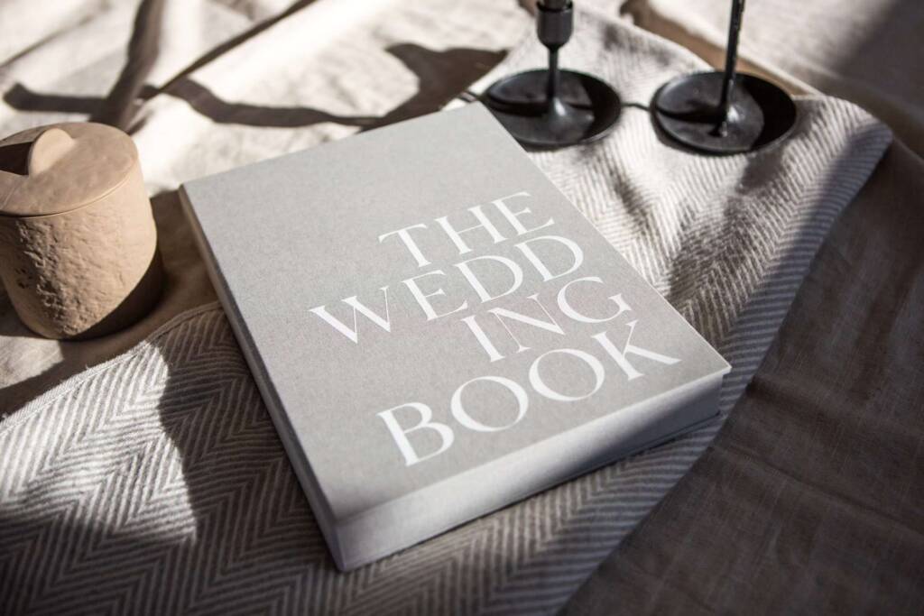 Landscape image of a grey photo album slipcase with bold white cover printing on a cream rug and herringbone blanket.
