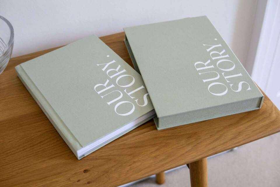 A pistachio coloured slipcase and coffee table photo book on a wooden table